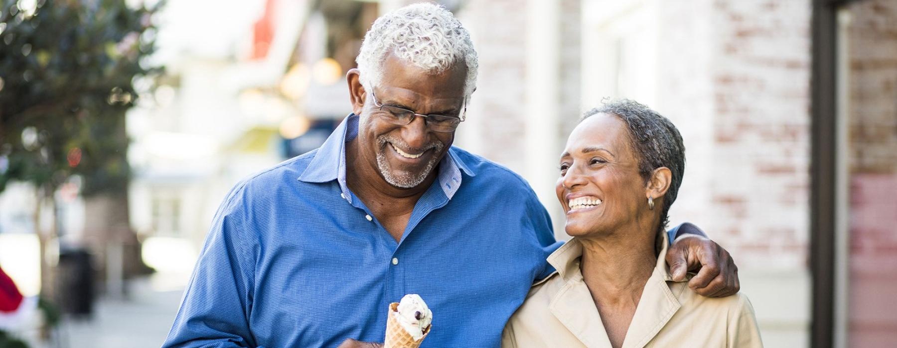 older couple walks down city sidewalk while holding ice cream cones